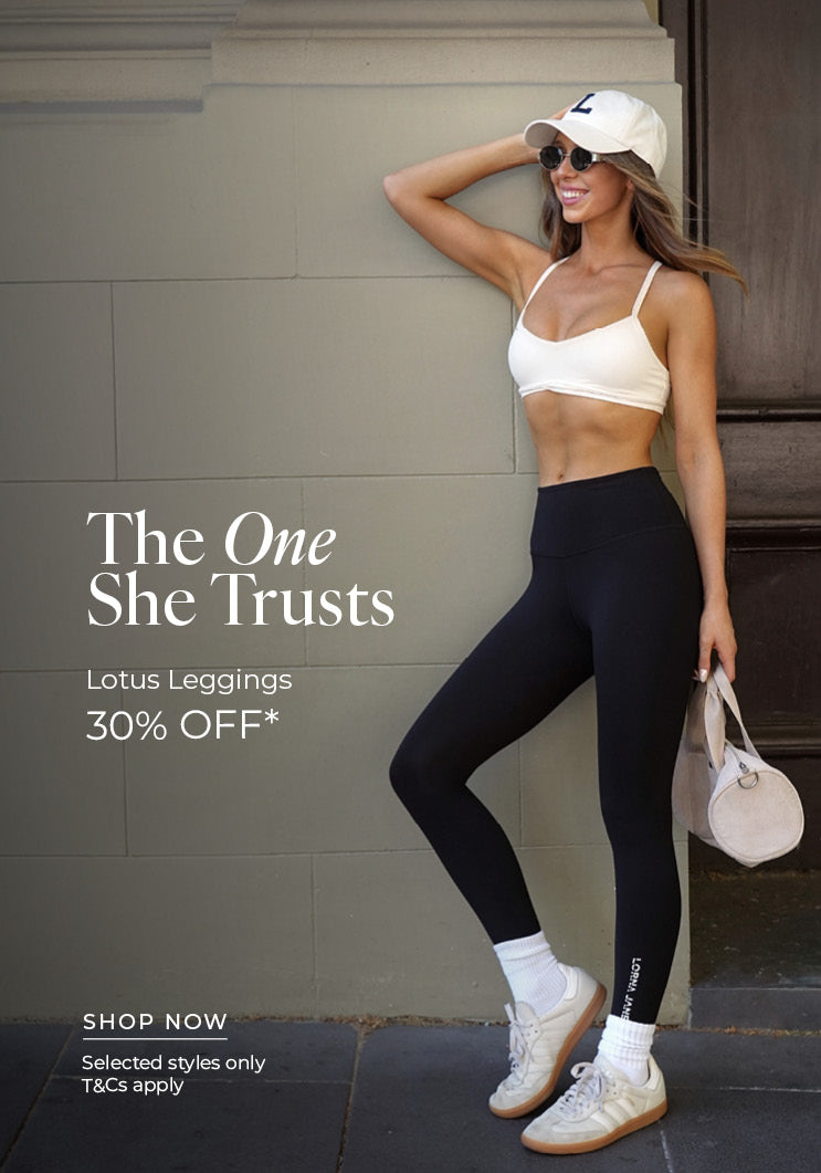 Woman leaning against a sage-green wall in black Lotus Leggings, a white sports bra, white cap, sunglasses, white crew socks and sneakers, holding a small cream duffle bag. Text: The One She Trusts Lotus Leggings 30% Off* Selected styles only. T&Cs apply - Shop Now
