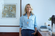 Lorna Jane Clarkson standing in front of a painting wearing a blue striped sports bra and long sleeve button up shirt
