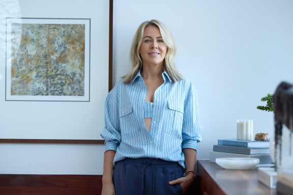 Lorna Jane Clarkson standing in front of a painting wearing a blue striped sports bra and long sleeve button up shirt
