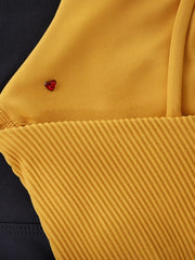 Close-up of a mustard yellow ribbed Lorna Jane garment featuring a small red heart-shaped bead detail.