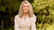 Lorna Jane Clarkson wearing a beige jacket sitting in a field with long grass