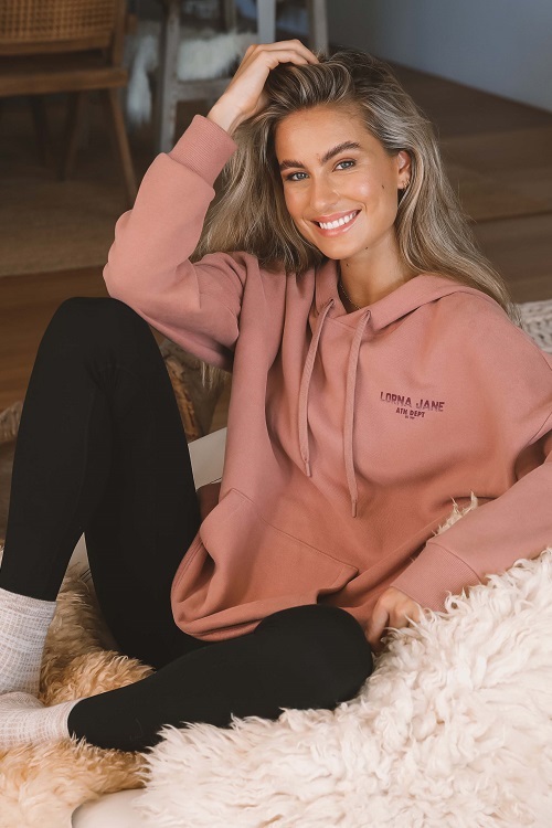 blonde woman sitting on a rug wearing black fleece-lined leggings and a brown oversized hoodie