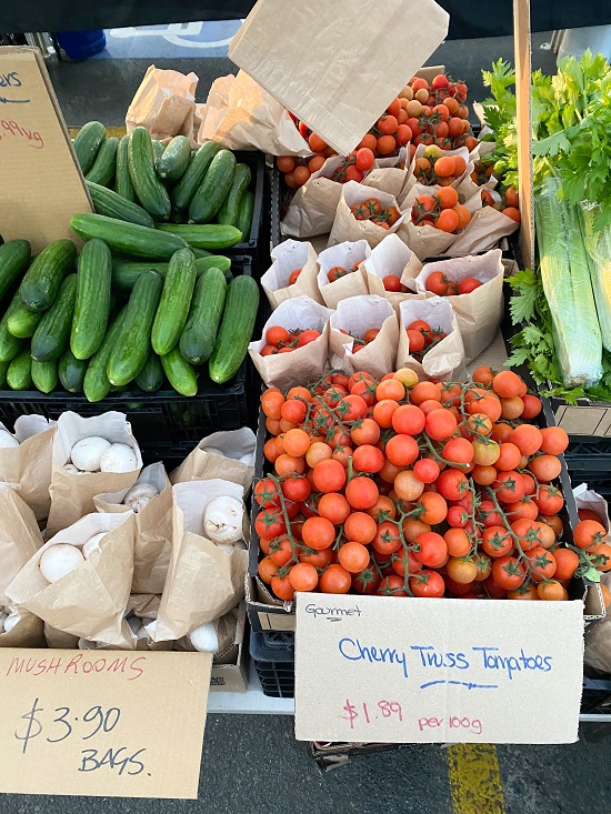a variety of fresh organic vegetables on a table at a farmers market including cucumber, cherry tomatoes and mushrooms