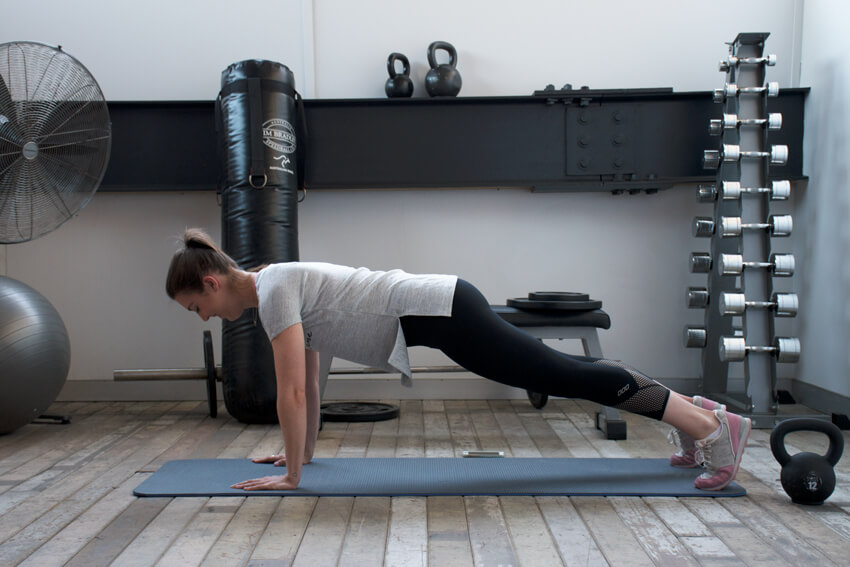 woman wearing grey tee and black ankle biter leggings doing best arm workouts for summer plank with arm extensions