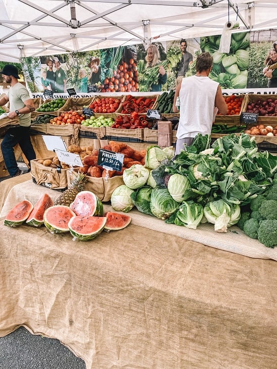 a variety of fresh organic vegetables on a table at a farmers market including watermelon, lettuce, cauliflower