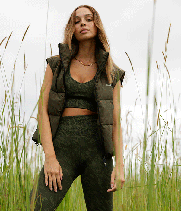 woman wearing army print leggings and sports bra with a khaki green puffer vest